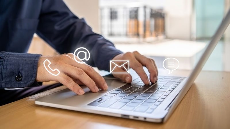 Business professional typing on a laptop with icons for phone, email, and chat communication, symbolizing multichannel customer service solutions.