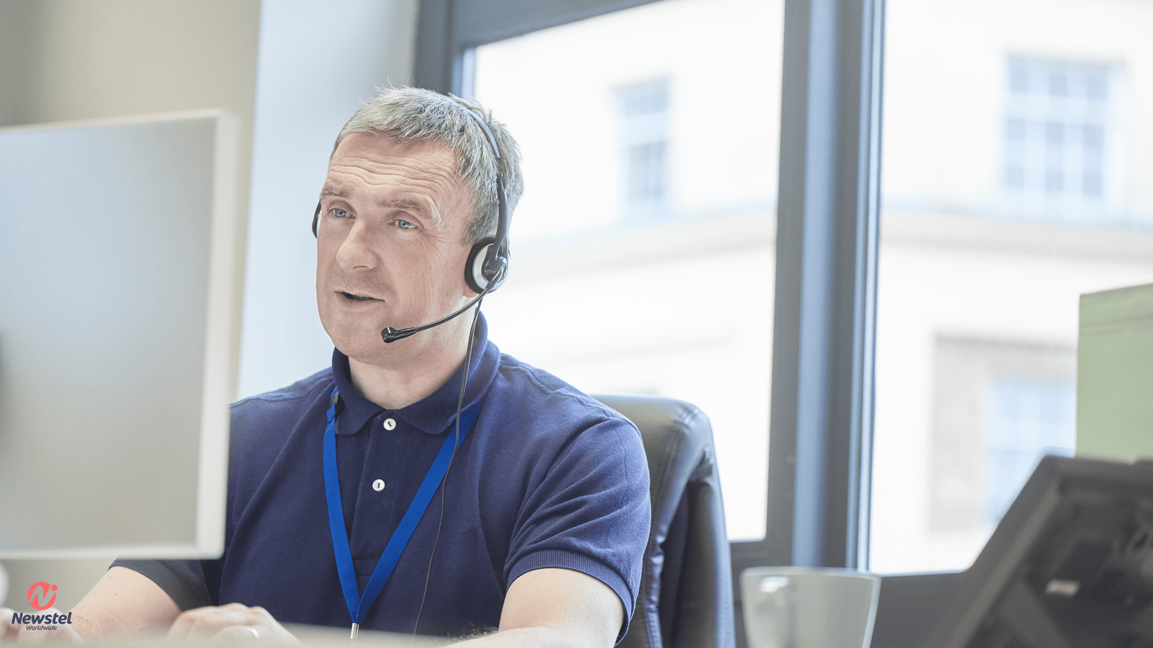Experienced customer support agent wearing a headset and blue lanyard, attentively engaging with a customer on his computer while providing multilingual support solutions.