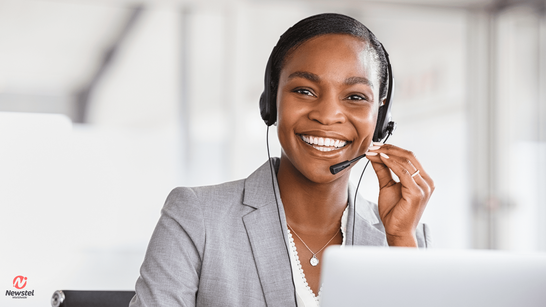 A smiling customer service representative wearing a headset, looking at her laptop screen while providing multilingual customer support solutions.