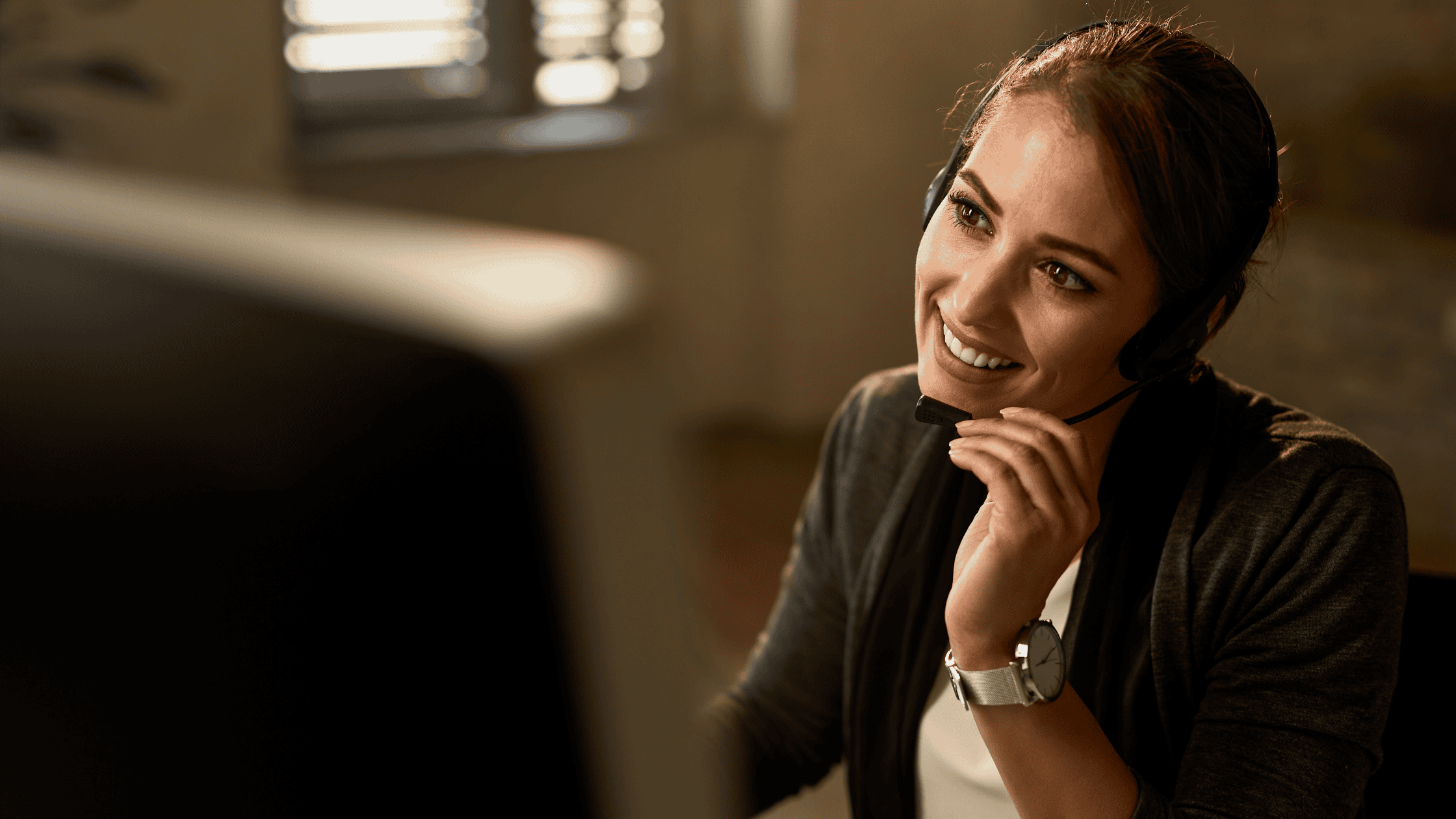 A smiling female support agent wearing a headset and assisting a customer from her workstation