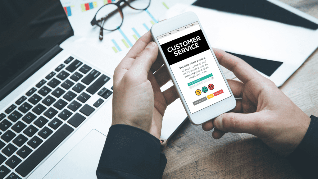 A mobile phone displaying a customer service interface, held in a professional setting near a laptop and documents