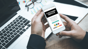 A mobile phone displaying a customer service interface, held in a professional setting near a laptop and documents