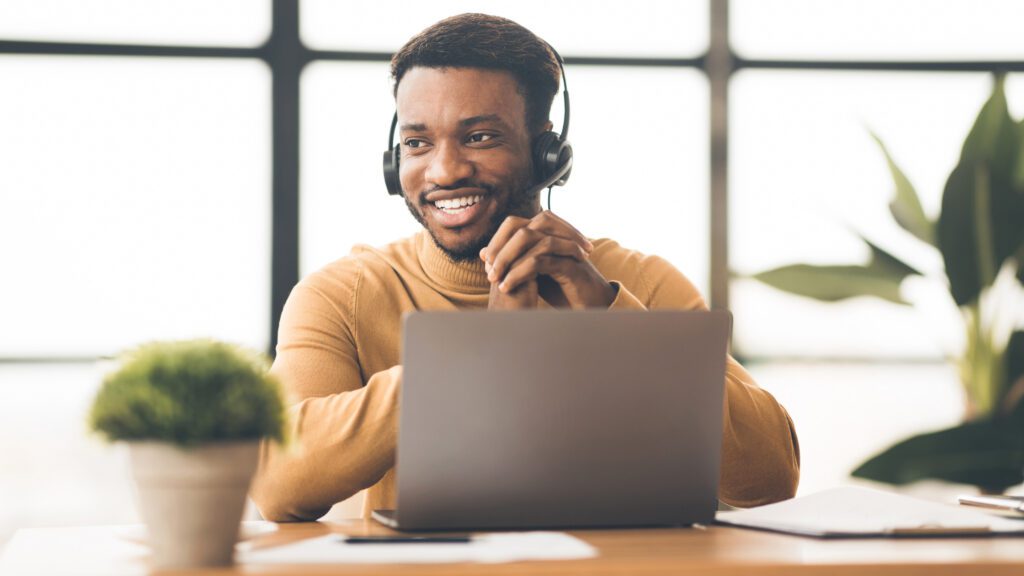 Smiling support specialist providing multilingual phone support 24/7 from a modern workspace.