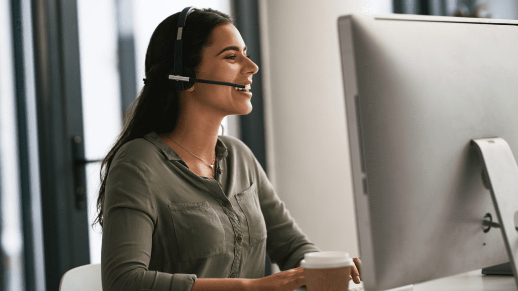 A customer care agent with a headset smiling while working, representing multilingual customer care round clock.