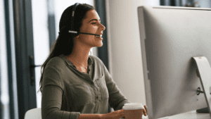 A customer care agent with a headset smiling while working, representing multilingual customer care round clock.