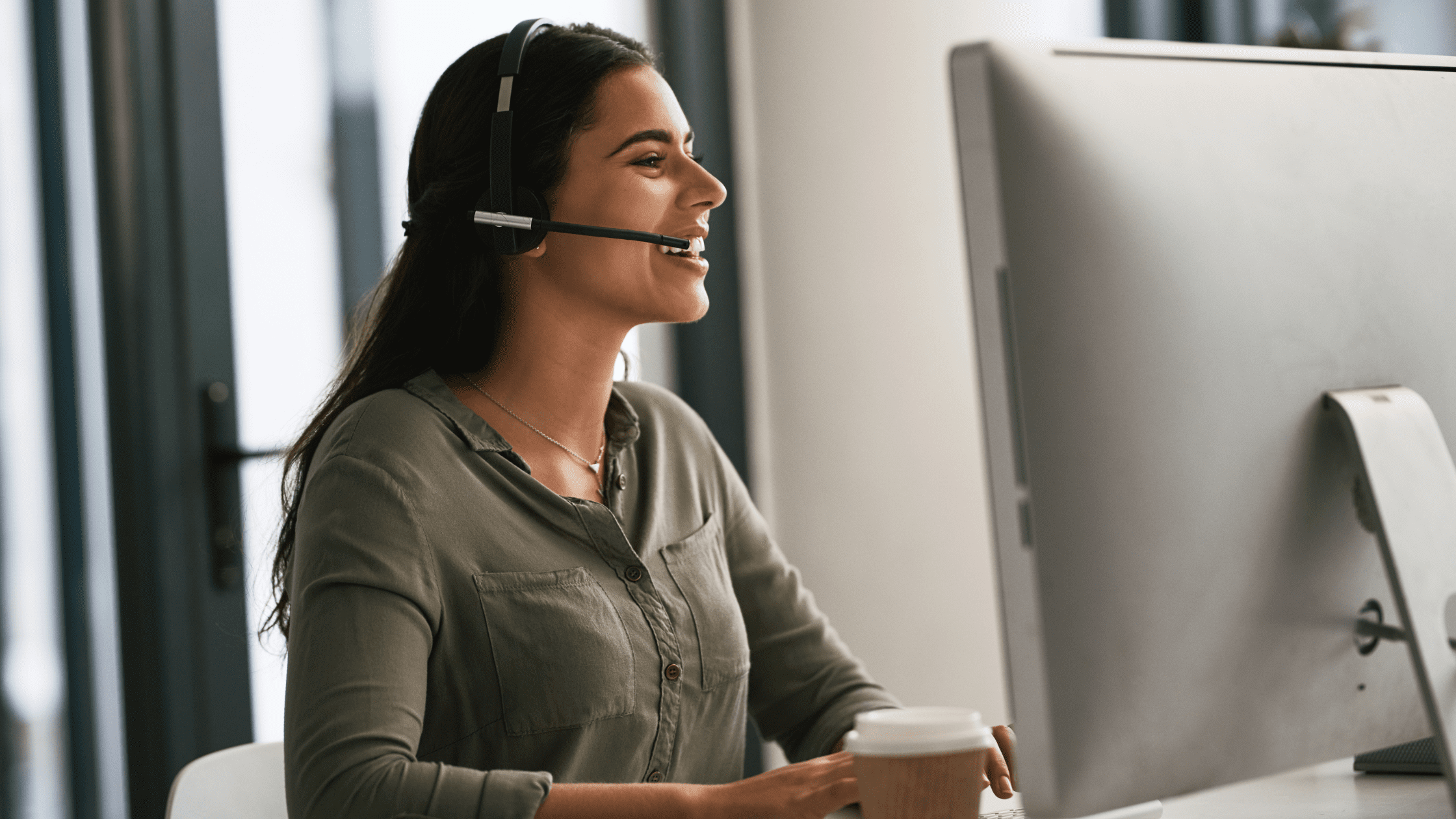 A customer care agent with a headset smiling while working, representing multilingual customer care round clock.