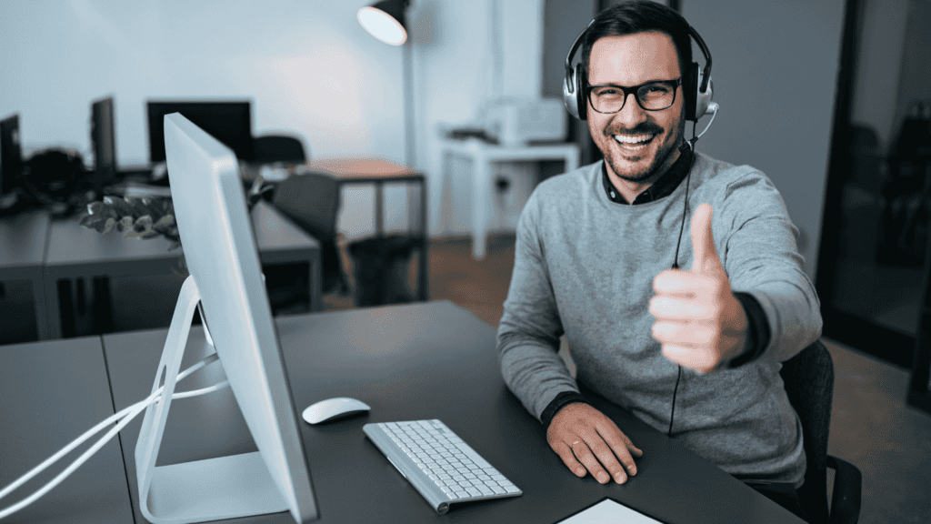 A smiling customer support agent giving a thumbs up while wearing a headset and sitting at a computer, symbolizing efficient and positive back-office support.