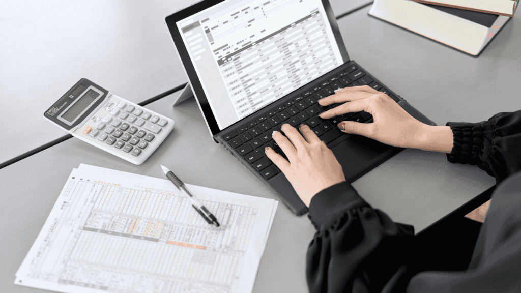 A professional working on financial data using a tablet, with spreadsheets, documents, and a calculator on the desk.