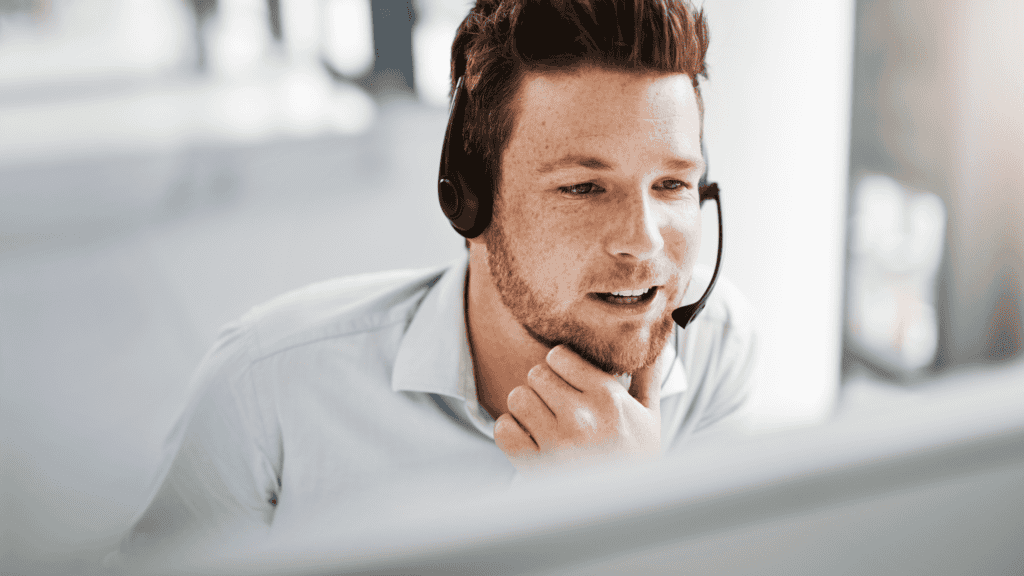 A male customer support agent with a headset, smiling while assisting a client.