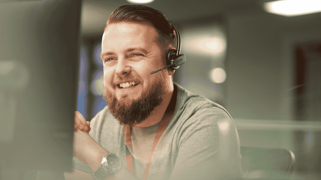 A smiling male customer support representative wearing a headset in a professional office setting.