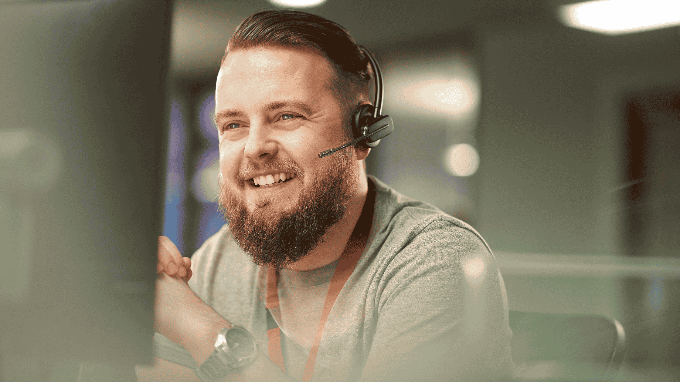 A smiling male customer support representative wearing a headset in a professional office setting.