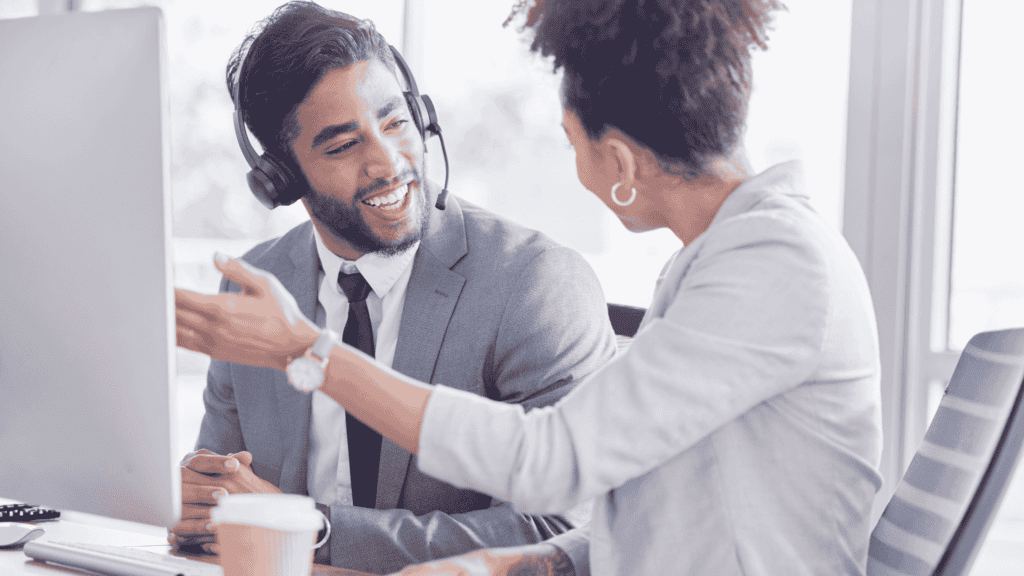 Two professionals collaborating in an office while wearing headsets, discussing customer service solutions.