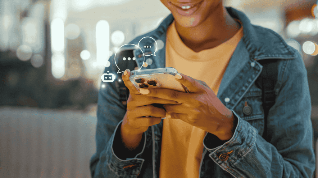 A person holding a smartphone with chat bubbles and a chatbot icon illuminated around the device.