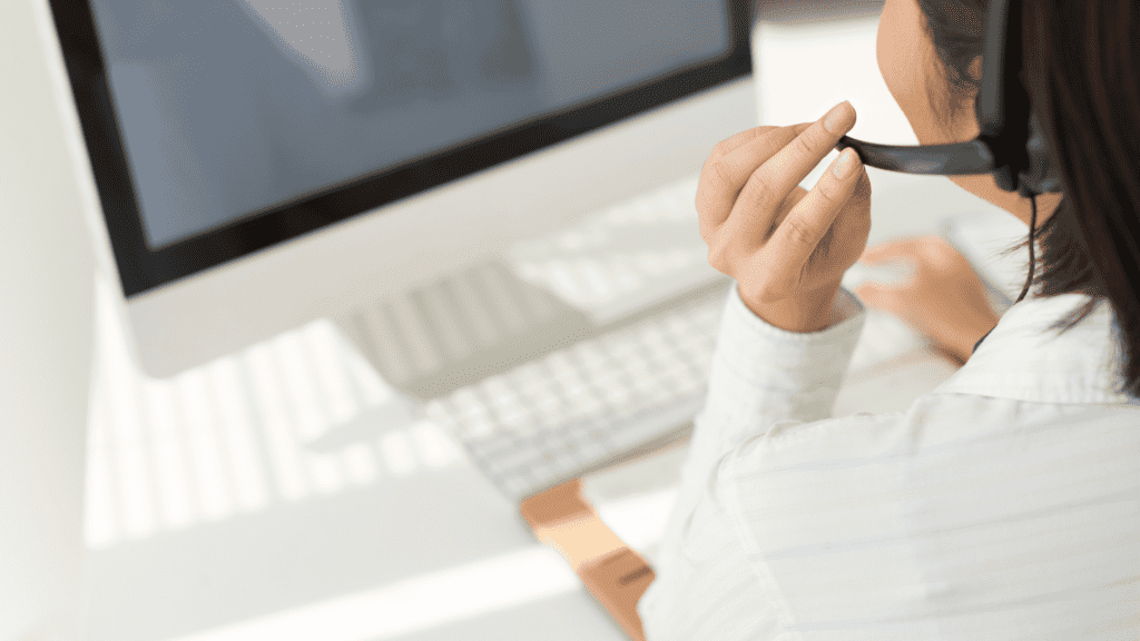 A customer service representative wearing a headset and working on a desktop computer in a brightly lit office.