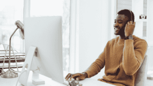 A smiling customer service representative wearing a headset, working at a desktop computer in a bright, modern office.