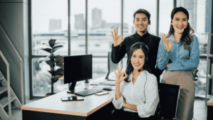 A team of multilingual support professionals showing an 'OK' hand gesture in a modern office environment.