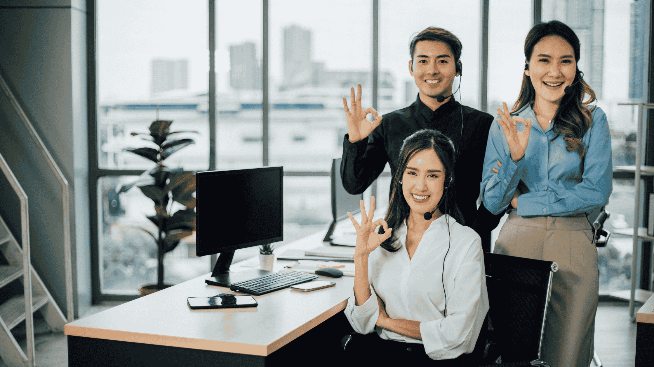 A team of multilingual support professionals showing an 'OK' hand gesture in a modern office environment.