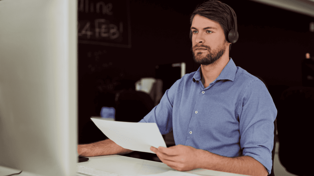 A focused professional wearing a headset, analyzing a document at their workstation.