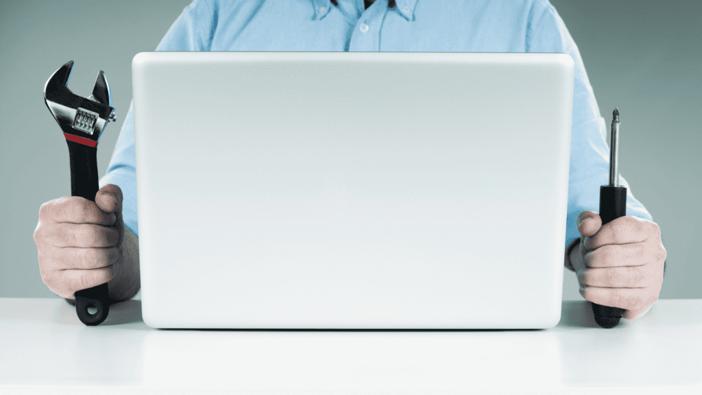A person holding a wrench and screwdriver in front of a laptop, symbolizing IT support and troubleshooting.