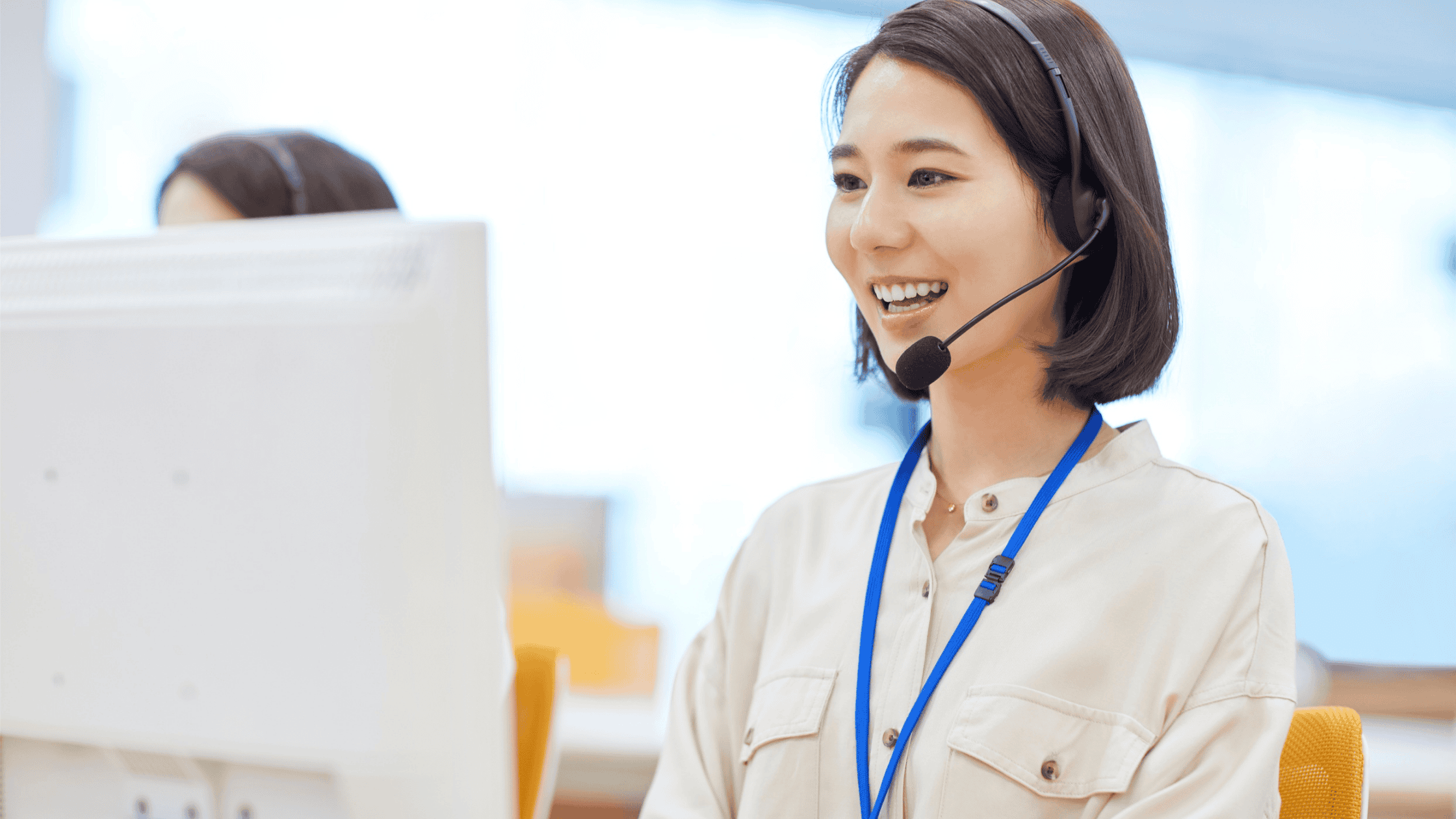 Smiling female customer service representative wearing a headset, engaging in a conversation at her workstation.