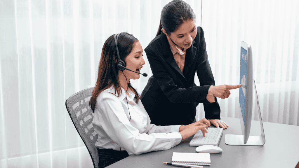 A supervisor assisting a customer support representative at a computer, demonstrating professional multilingual back-office support.