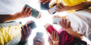 Group of Gen Z individuals standing in a circle, holding smartphones and looking down at their screens.