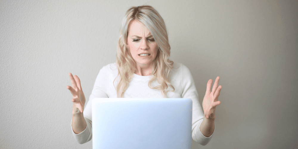 Frustrated woman looking at laptop, raising hands in anger, symbolising poor online shopping experience and customer support failures in UK retail.