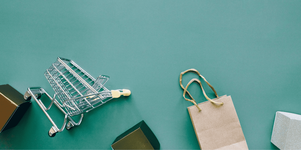 Minimalist e-commerce concept showing a tipped shopping trolley, a paper bag, and gift boxes on a green background, symbolising UK retail CX struggles and delivery failures.