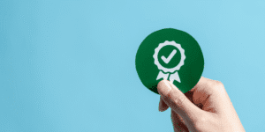 Hand holding a green badge with a tick icon symbolising compliance and service quality.