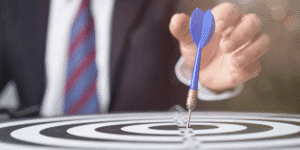 Businessman in a suit aiming a blue dart at the bullseye of a target, symbolising BPO focus and precision.