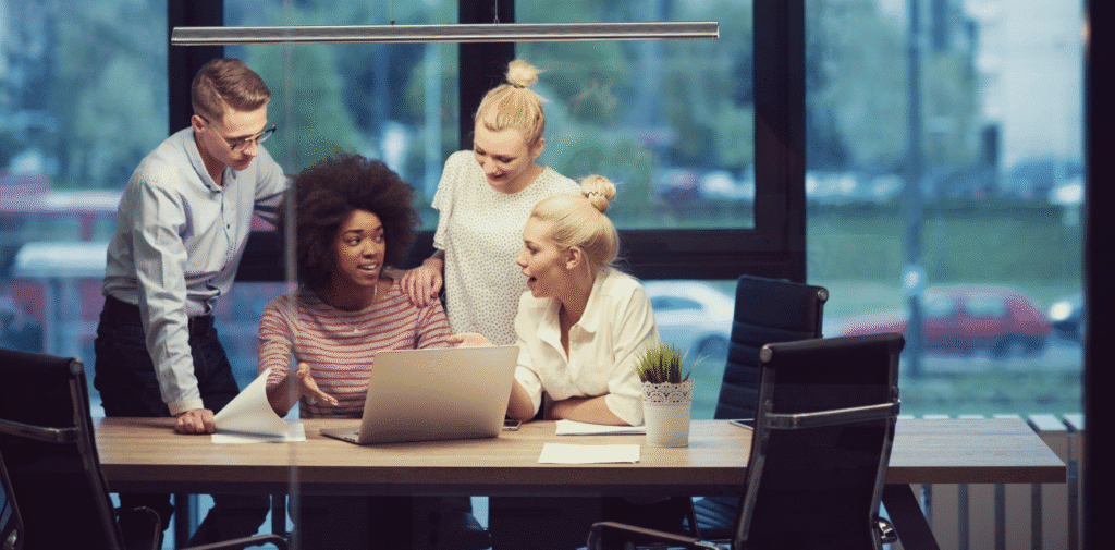 Four team members gather around a laptop in a modern office while discussing scalable and budget-friendly customer support strategies.